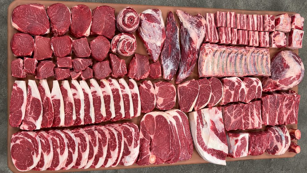 A half beef share laid out on the board: rows of ribeyes, strips, short ribs, roasts and ground beef, seen from above